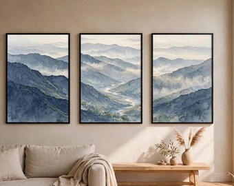 May include: A triptych of three vertical framed wall art prints featuring a watercolour landscape of blue and grey mountain ranges with misty valleys and a winding river, all enclosed in thin black frames displayed in a row on a wall.