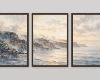 May include: A triptych of three framed vertical wall art prints depicting a coastal landscape. The watercolour-style artwork shows rocky cliffs partially obscured by mist, meeting a calm ocean under a soft, pale, and cloudy morning sky.