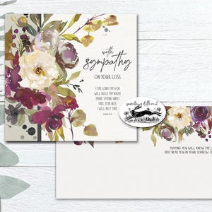 May include: A sympathy card set with a watercolour floral design. The card features a bouquet of white, purple, and burgundy flowers. Text reads "With sympathy on your loss" and a verse. An oval sticker with a running hare is included.