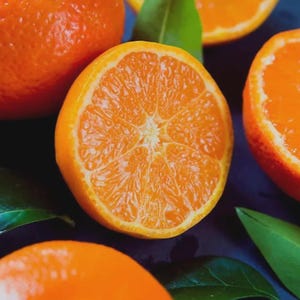 May include: A bright orange mandarin orange cut in half, revealing the juicy, segmented interior flesh. The fruit is surrounded by several whole mandarin oranges and vibrant green leaves, showcasing the textured peel and pulp structure.
