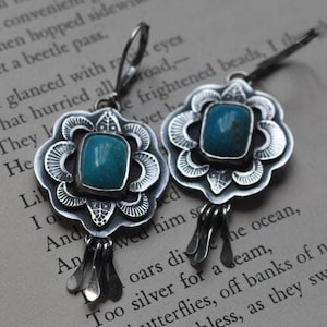 Puede incluir: Un par de pendientes de plata con piedras turquesa engastadas en un diseño floral. Los pendientes tienen un borla colgante.