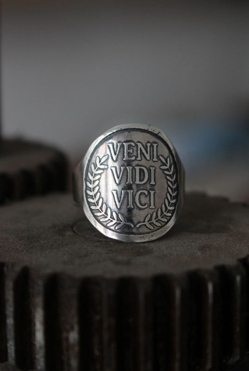 May include: A silver ring with a laurel wreath design and the inscription "VENI VIDI VICI" on the face.