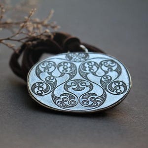 May include: A silver pendant with an intricate Celtic knot design. The pendant is round and has a smooth, polished finish.