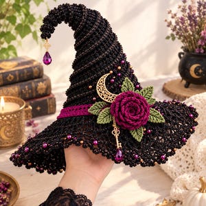May include: A black crocheted pointed hat featuring a purple rose, green leaves, a gold crescent moon charm, and a hanging gold key with a purple teardrop crystal. The hat is adorned with small purple and gold beads throughout the fabric.