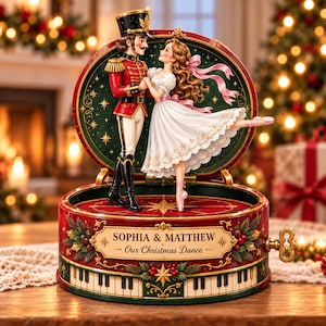 Può includere: Un carillon rotondo con uno schiaccianoci e una ballerina che danzano. La base è rossa con un motivo a tasti di pianoforte, decorazioni di pino verde e il testo SOPHIA & MATTHEW Our Christmas Dance. Una chiave di carica dorata è sul lato.