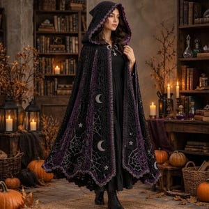 Può includere: Un mantello nero con cappuccio caratterizzato da intricati motivi all'uncinetto, bordi viola e decorazioni argentate a forma di mezzelune, stelle e ragnatele. Il capo presenta un bordo smerlato e una chiusura in metallo sullo scollo.