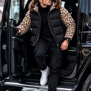 Può includere: Un gilet imbottito con busto trapuntato nero, maniche con stampa leopardata e cappuccio bordato in pelliccia sintetica marrone. Indossato sopra un maglione a collo alto nero, abbinato a pantaloni cargo neri e sneakers bianche alte.