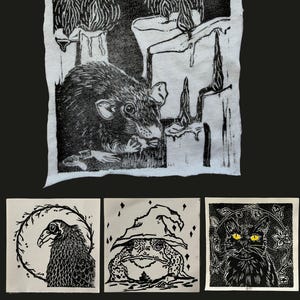 May include: Four black and white linocut prints on fabric. The top print shows a rat near melting candles. The bottom row features a bird in a wreath, a toad wearing a pointed hat, and a cat with yellow eyes surrounded by floral vines.