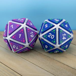 May include: Two twenty-sided dice with a white frame structure. One die is purple with pink star-shaped accents and white numbers, while the other is blue with green star-shaped accents and white numbers. Each face is a triangle with clear numbering.
