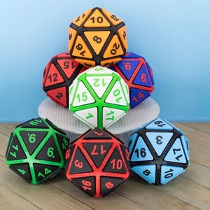 May include: A collection of seven twenty-sided dice arranged in a pyramid formation. Each die features a black frame with colored triangular faces, including orange, red, blue, white, green, and light blue, all displaying black or colored numbers.