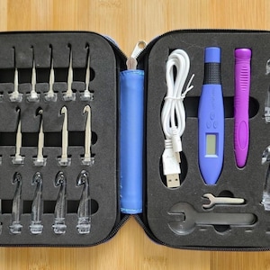 May include: A black zippered carrying case containing a set of crochet hooks and tools. The kit includes metal hooks, clear plastic hooks, a purple handle, a blue digital handle with an LCD screen, a white USB charging cable, and two metal wrenches.