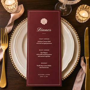 May include: A deep burgundy dinner menu card featuring a white border, a wax seal monogram at the top, and text listing courses including Heirloom Tomato Salad, Filet Mignon, and Vanilla Bean Crème Brûlée for Eleanor and James, June 12, 2027.
