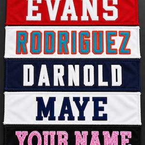 May include: Five rectangular fabric patches with embroidered lettering. The top patch is red with white text EVANS. The second is white with blue and orange text RODRIGUEZ. The third is navy with white text DARNOLD. The fourth is white with navy text MAYE. The bottom is black with pink glitter text YOUR NAME.