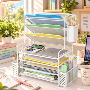 May include: A white metal mesh desk organizer featuring three vertical file slots with blue, green, and yellow folders, a flat shelf holding a calculator and tablet, and side compartments containing pens, pencils, and scissors. The unit includes horizontal trays for notebooks and books.