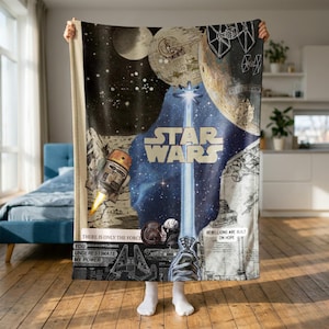 Könnte beinhalten: Eine Star Wars Fleecedecke mit einem zentralen Lichtschwertstrahl, dem Star Wars Logo, einem Droiden, TIE-Jägern und Planeten. Das Design enthält Texte wie There is only the force, You underestimate my power und Rebellions are built on hope vor einem dunklen Weltraumhintergrund mit verschiedenen technischen Illustrationen.