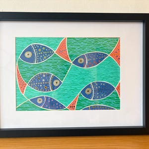 May include: A framed art print featuring a stylised illustration of blue fish with yellow and white polka dots swimming through a vibrant green sea. The background consists of wavy lines, and the fish have coral-coloured fins and tails.