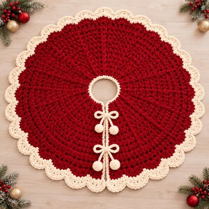 May include: A circular, deep red crocheted tree skirt featuring a thick, cream-colored scalloped border. The center has a circular opening with two cream-colored ties, each finished with a small pom-pom, to secure the skirt around a tree base.
