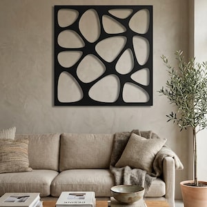 May include: A square black wall art piece featuring an organic, cutout pattern of interconnected, rounded, pebble-like shapes. The design consists of a solid frame with varying sizes of open voids, creating a geometric, lattice-like structure.