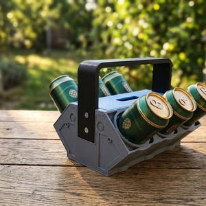以下が含まれることがあります： 黒いハンドルが付いたグレーのプラスチック製ドリンクキャリアで、6本の緑色のアルミ缶を収納しています。このキャリアは幾何学的な工業デザインで、ハンドルをベースに固定するネジが見えており、標準サイズのドリンク缶を保持するように設計されています。