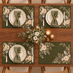Peut inclure: Un ensemble de quatre sets de table rectangulaires vert foncé ornés d'un motif botanique de fleurs blanches, de baies bleues et de petits oiseaux. Chaque couvert comprend une assiette blanche, une serviette vert sauge et des couverts.