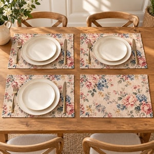 Peut inclure: Un ensemble de quatre sets de table rectangulaires arborant un motif floral avec des fleurs roses, bleues et jaunes sur un fond beige clair. Chaque set est disposé avec une assiette en céramique blanche, une fourchette et un couteau en argent.