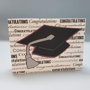May include: A graduation card with a black and gray graduation cap on a beige background with the word "Congratulations" repeated in black and red.
