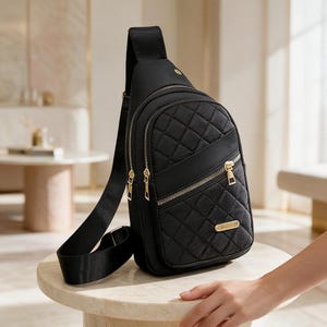 May include: A black quilted sling backpack featuring a vertical design with multiple zippered compartments, gold-toned hardware, and an adjustable shoulder strap. The front panel displays a diamond-stitched pattern and a small rectangular metal logo plate.