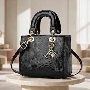 Puede incluir: Un bolso de mano negro con acabado brillante de textura de piel de serpiente, que presenta un cuerpo rectangular estructurado, un asa superior arqueada y lisa, y una correa de hombro desmontable. Incluye herrajes dorados y un dije colgante.
