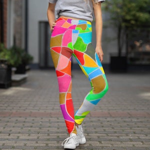 May include: A woman wearing a grey t-shirt and colourful leggings with a geometric pattern. The leggings are made of a stretchy fabric and have a high waist.