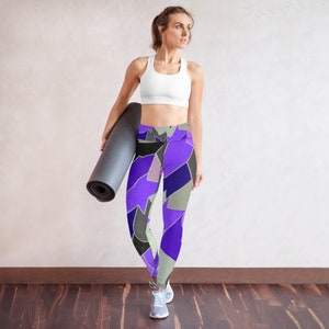 May include: A woman wearing a white sports bra and purple, black, and gray patterned yoga pants. She is holding a black yoga mat.