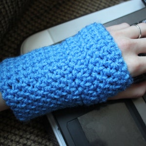 May include: A close-up of a blue crocheted wrist warmer. The wrist warmer is on a person's arm and the person's hand is resting on a laptop keyboard.