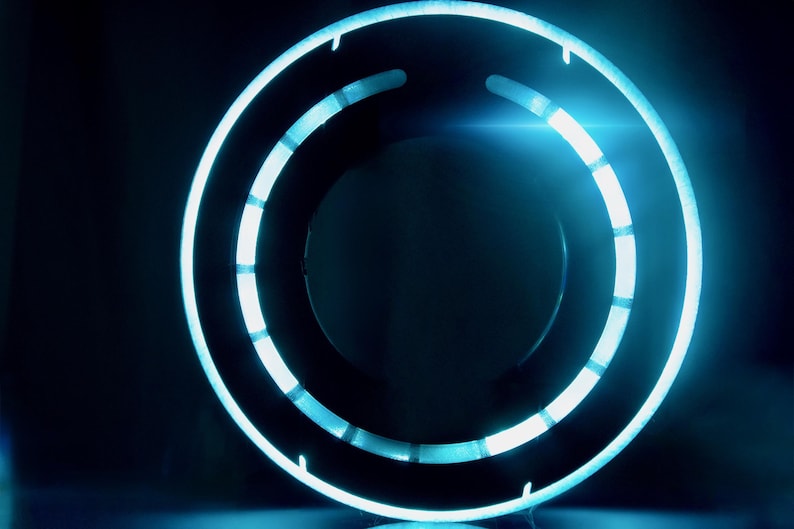 May include: A circular light fixture featuring a glowing cyan neon ring with segmented illumination. The design consists of a solid outer ring and an inner ring with distinct light gaps, creating a bright, high-contrast blue circular display.