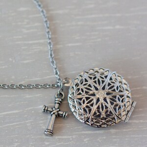 May include: Silver chain necklace with a filigree locket and a cross charm.