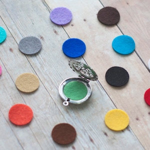 May include: A silver locket with a filigree design, open to reveal a green felt pad. Surrounding the locket are 13 felt circles in various colors, including pink, blue, red, yellow, brown, and gray.