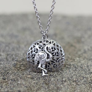 May include: Silver necklace with a round pendant featuring a delicate, intricate design and a flamingo silhouette.