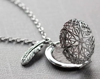 May include: A silver necklace with a delicate feather charm and a filigree locket that opens. The locket is open and the inside is visible.
