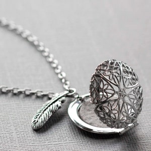 May include: A silver necklace with a delicate feather charm and a filigree locket that opens. The locket is open and the inside is visible.