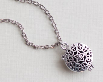 May include: A silver chain necklace with a round, openwork pendant. The pendant has a delicate floral design.