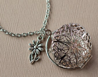 May include: A silver necklace with a delicate flower charm and a filigree cage pendant. The cage pendant is open and has a detailed design.