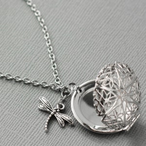 May include: Silver locket necklace with a delicate dragonfly charm. The locket is open and features a filigree design.