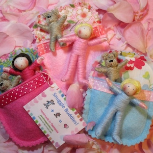 Könnte beinhalten: Vier handgefertigte Filzpuppen-Kuschelfreunde in rosa und blauen Schlafsäcken mit einem Etikett, auf dem "Snuggle Buddies! Handmade in Tasmania" steht.