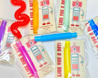 May include: A set of six Valentine's Day cards featuring a robot design and the text "I Like You A Bot!" Each card comes with a colourful plastic toy. The cards are packaged in clear plastic bags.