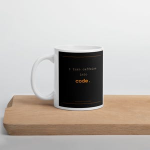Może przedstawiać: Biały ceramiczny kubek z czarną prostokątną grafiką z przodu. Napis "I turn caffeine into code." wykonano czcionką przypominającą maszynę do pisania, przy czym słowo "code." jest pomarańczowe. Pomarańczowe linie otaczają blok tekstu na kubku.