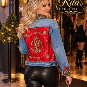May include: A blue denim jacket featuring a vibrant red satin back panel with a gold crown and chain print, a leopard print collar, and leopard print cuffs. The jacket is paired with black leather-look trousers and a black handbag.