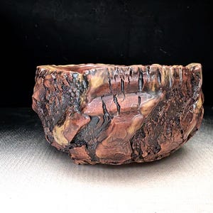 May include: A ceramic bowl with a textured exterior that mimics the appearance of rough tree bark. The surface features deep grooves and ridges in shades of dark brown, reddish-brown, and tan, creating a rugged, organic look with a glossy finish.