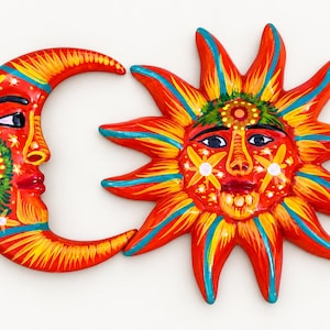 May include: A pair of wall plaques featuring a crescent moon and a sun, both painted in vibrant red, yellow, and turquoise colours. The moon and sun both have human-like faces with detailed floral and geometric patterns painted on their surfaces.