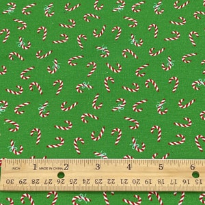 Pode incluir: Tecido verde com um padr&atilde;o repetido de bengalas doces vermelhas e brancas, algumas com pequenos la&ccedil;os azuis. Uma r&eacute;gua com medidas em polegadas na parte inferior. Ideal para trabalhos manuais de Natal.
