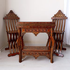 May include: A handcrafted wooden table and two chairs set. The furniture features intricate inlaid patterns in shades of brown, red, and beige. The chairs have a slatted back design. The table is approximately 30 inches long.
