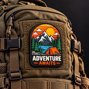 May include: A rectangular patch with rounded top corners attached to an olive green tactical backpack. The patch features a colourful graphic of a mountain range, a lake, pine trees, and an orange tent under a sun, with the text ADVENTURE AWAITS.