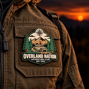 May include: A rectangular olive green jacket featuring a patch with a graphic of an off-road vehicle with a roof tent, pine trees, mountains, and a compass star. The text reads OVERLAND NATION ADVENTURE CLUB EST. 2023 in white lettering.